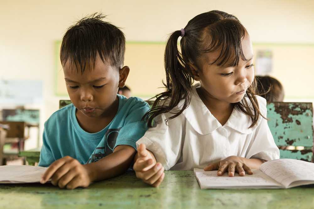 Kleiner Junge und Mädchen sitzen auf einer Schulbank und lesen